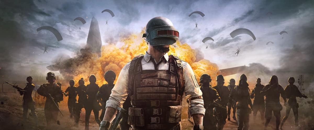 Visuel clé de PUBG: Battlegrounds : un soldat casqué en gilet tactique avance devant une foule de combattants, une explosion et des parachutes