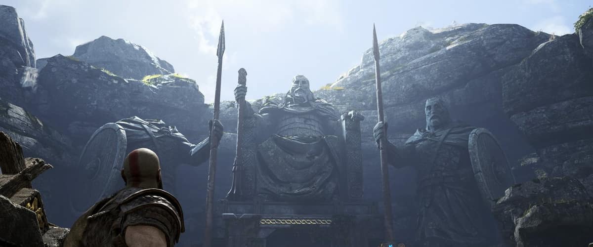 Kratos, de dos, face à deux statues géantes de guerriers armés de lances taillées dans la falaise