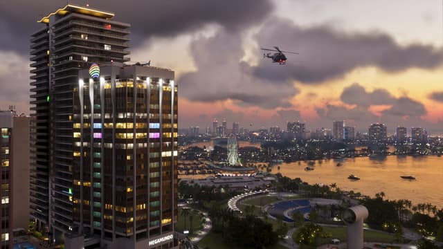 Tour d'hôtel illuminée et front de mer de Vice City au crépuscule, survolés par un hélicoptère