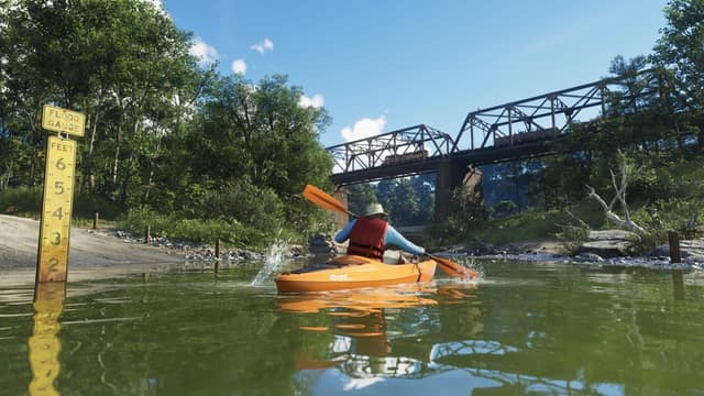 Un kayakiste descend une rivière sous un pont ferroviaire métallique dans le parc national du mont Kalaga