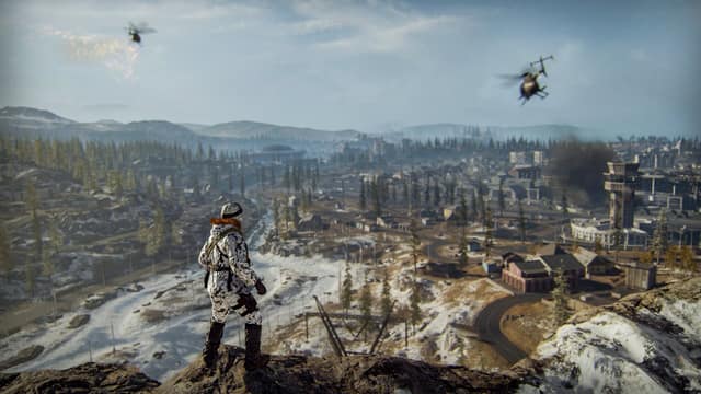 Un opérateur en tenue de camouflage hivernale observe depuis un rocher une ville survolée par des hélicoptères dans Call of Duty: Warzone