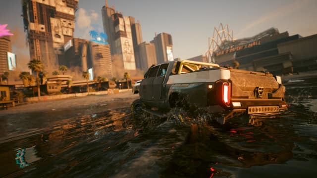 Un pick-up traverse une route inondée devant des immeubles et un centre commercial