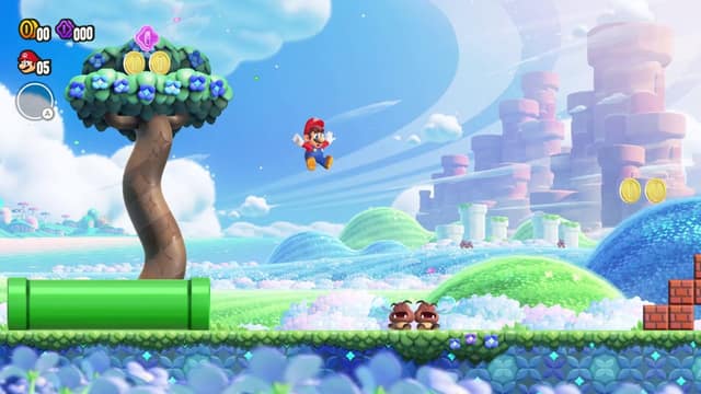 Mario saute au-dessus d'une plaine fleurie, près d'un tuyau vert et de deux Goombas, dans Super Mario Bros. Wonder
