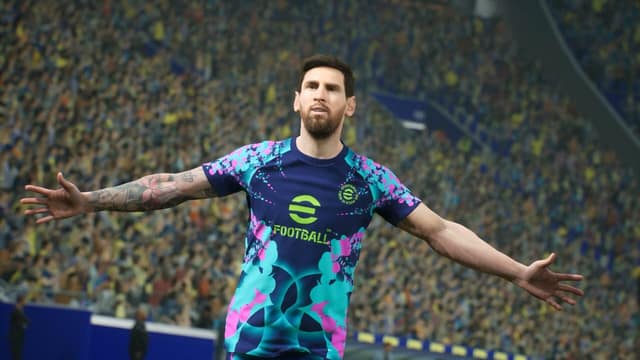 Un footballeur en maillot eFootball célèbre bras écartés devant une tribune pleine