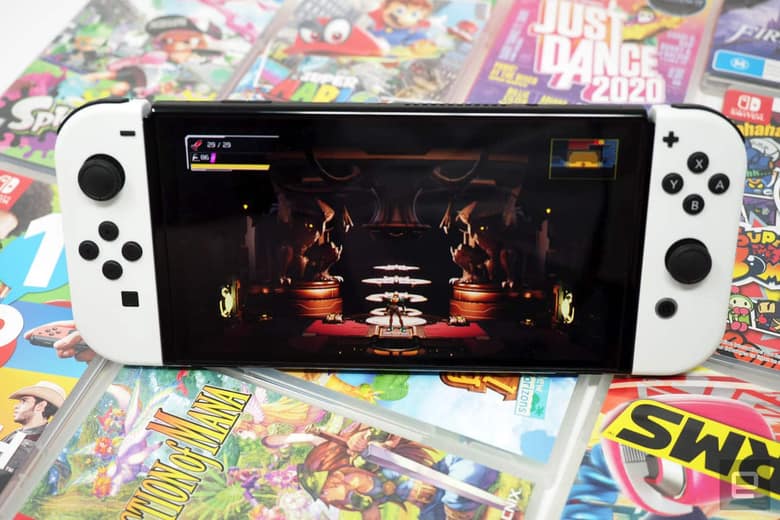 Nintendo Switch OLED en main au-dessus d'une pile de boîtes de jeux