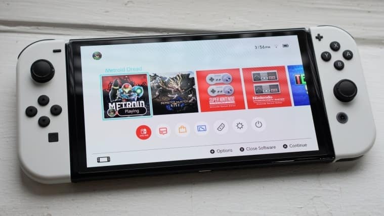 Nintendo Switch OLED posée à plat, écran d'accueil affiché, Joy-Con blancs