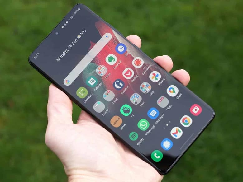 Un Samsung Galaxy S21 Ultra en main au-dessus d'une pelouse, écran d'accueil affiché