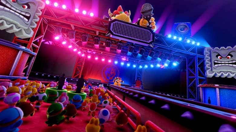 Scène d'un plateau de télévision géant, éclairée de néons roses et bleus, avec Bowser au micro face à un public de Toad et de Yoshi