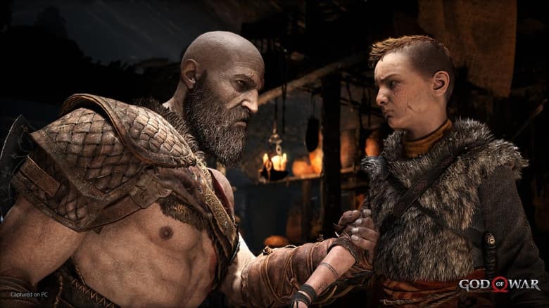 Kratos pose la main sur le bras de son fils Atreus, dans une maison éclairée à la bougie
