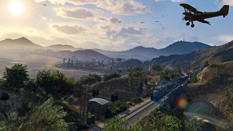 Un avion épandeur jaune survole les collines de GTA 5 au coucher du soleil, au-dessus d'un train de marchandises