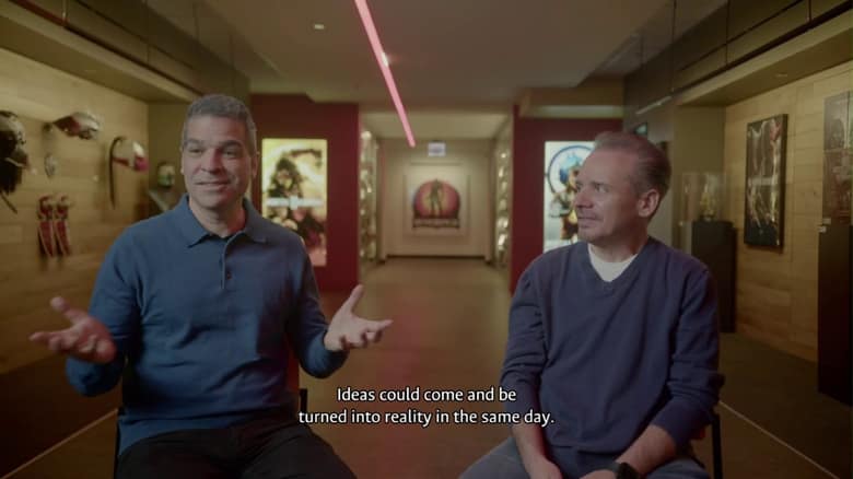 Deux créateurs de Mortal Kombat interviewés dans un couloir décoré d'affiches de la série