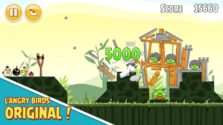 Capture officielle de Rovio Classics: Angry Birds : une construction en bois écroulée sur des cochons casqués, un gain de 5 000 points affiché et le texte « L'Angry Birds original ! »