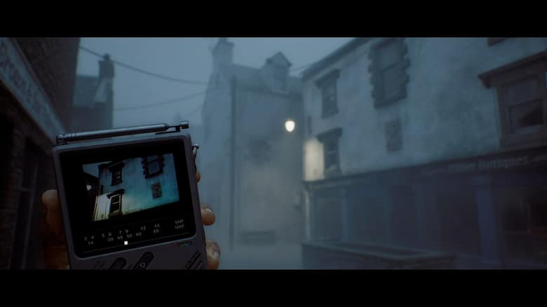 Capture officielle de Silent Hill: Townfall : une main tient un petit téléviseur de poche allumé dans une rue de village écossais noyée dans le brouillard
