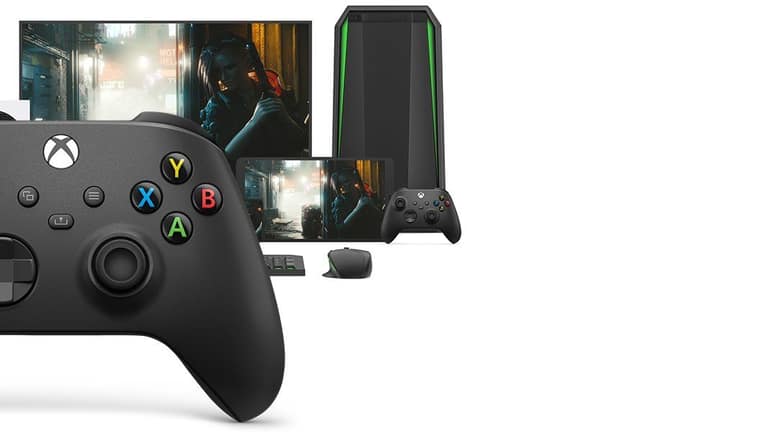 Une manette sans fil Xbox noire devant un écran, une tour de PC et un téléphone